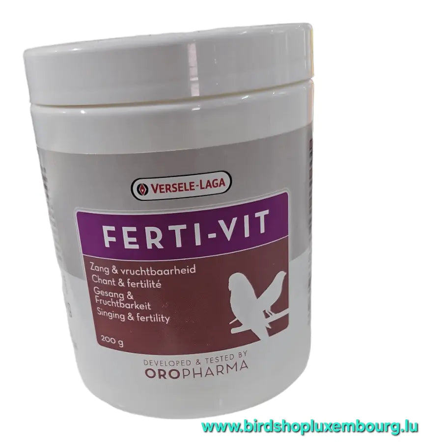 Un récipient blanc étiqueté « Ferti-Vit 200GR » de Versele-Laga présente un design violet et orange avec une silhouette d'oiseau. Il met en valeur le chant et la fertilité, enrichi en vitamine E, mettant en valeur le savoir-faire de Versele-Laga. Une adresse de site Web est visible en bas.