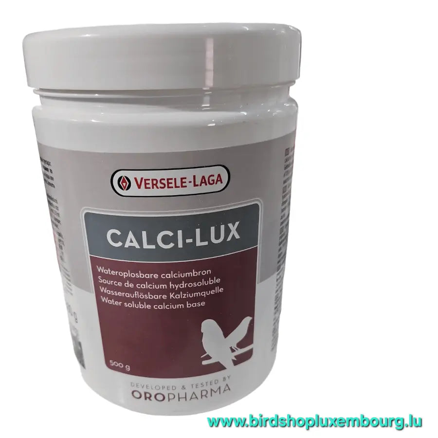 Un contenant blanc de Versele-Laga CALCI-LUX 500GR, un complément de calcium hydrosoluble pour animaux de compagnie, permet de remédier à la carence en calcium. Il présente une silhouette d'oiseau et comporte un texte multilingue avec l'URL d'un site Web en vert en bas.